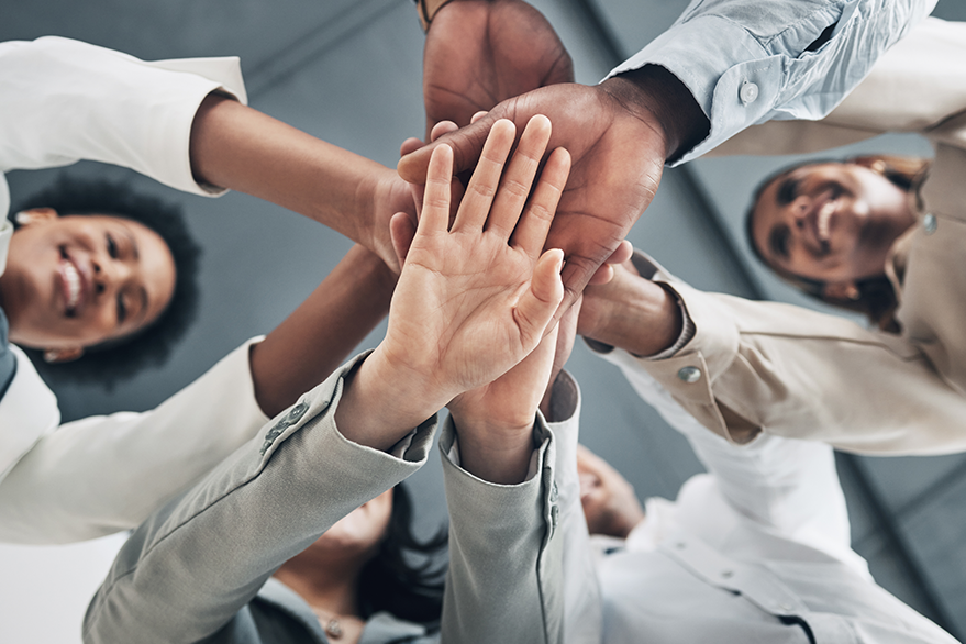 Arbeitskolleginnen und Kollegen, die im Kreis stehen und ihre Hände übereinander halten.