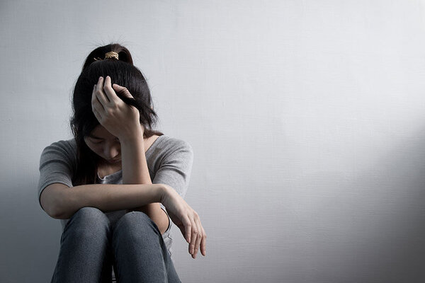 Eine Frau sitzt traurig auf dem Boden, das Gesicht auf ihrer Hand abgestützt